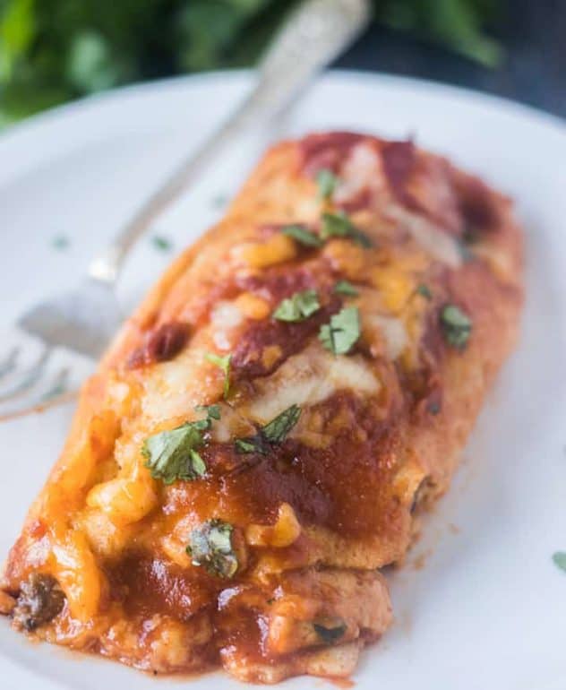 Enchilada on a white place with a silver fork and garnished with cilantro.