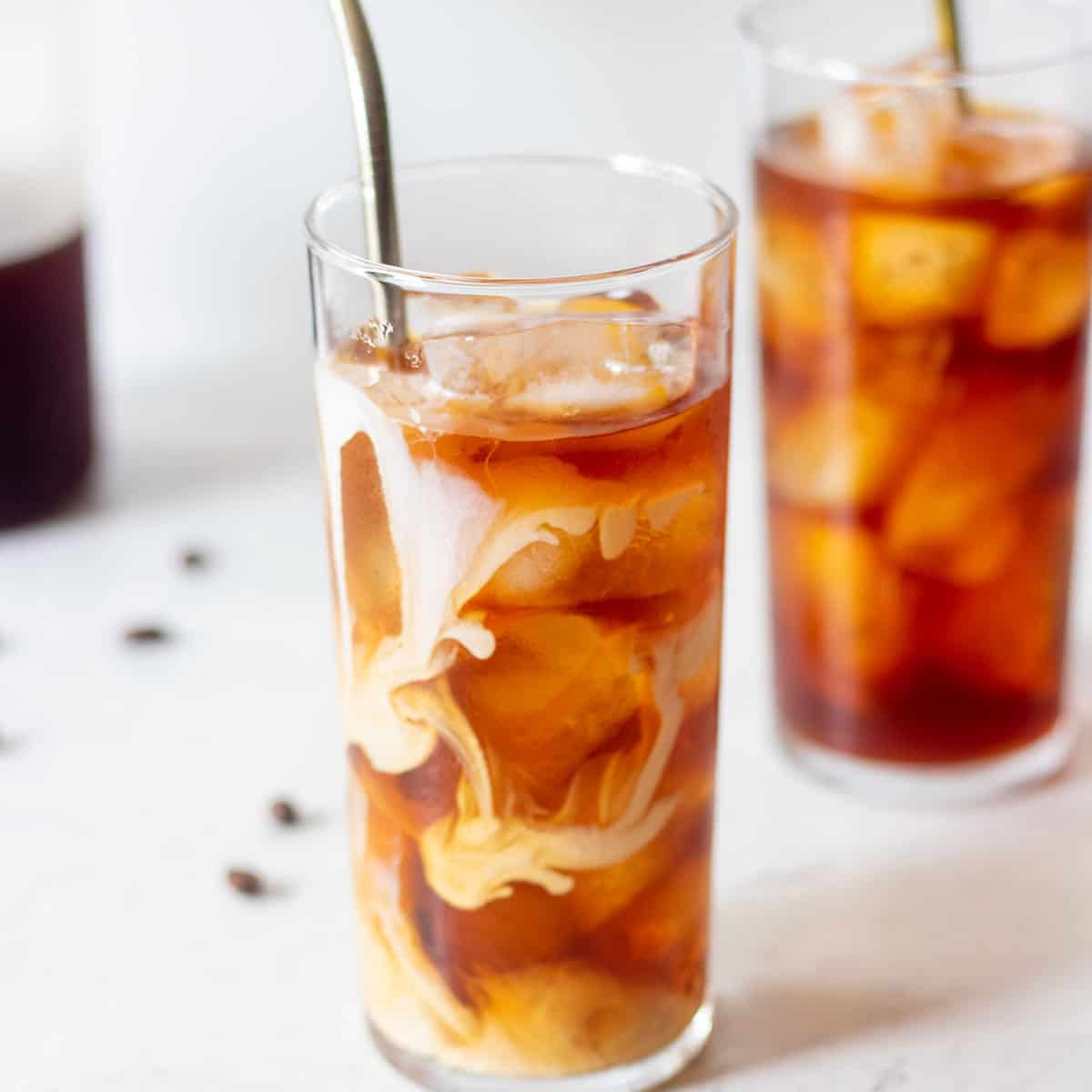 cold brew coffee in a clear glass with half and half cream, ice and a stainless steel straw.