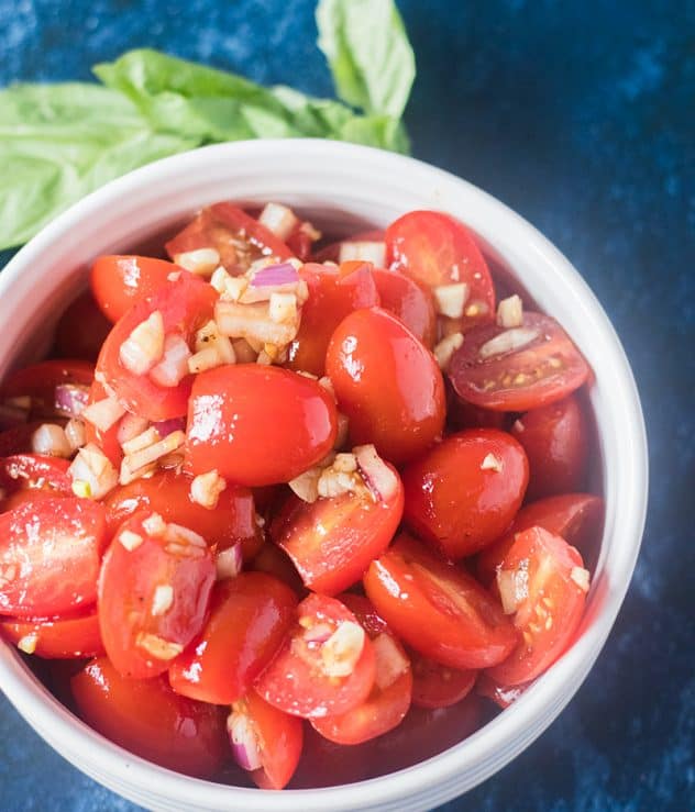 Fresh cherry tomatoes mixed with garlic, red onion, olive oil and balsamic vinegar in a bowl.