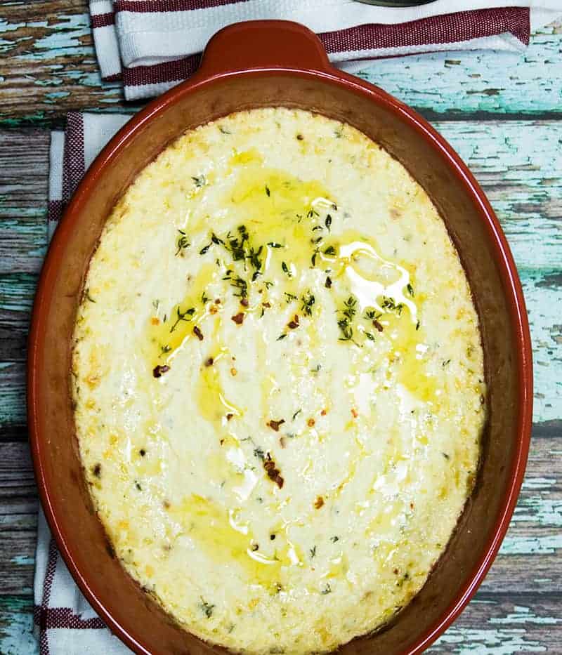 Lemon Thyme Baked Ricotta Cheese in a red oval baking dish garnished with fresh thyme and red chili pepper flakes.