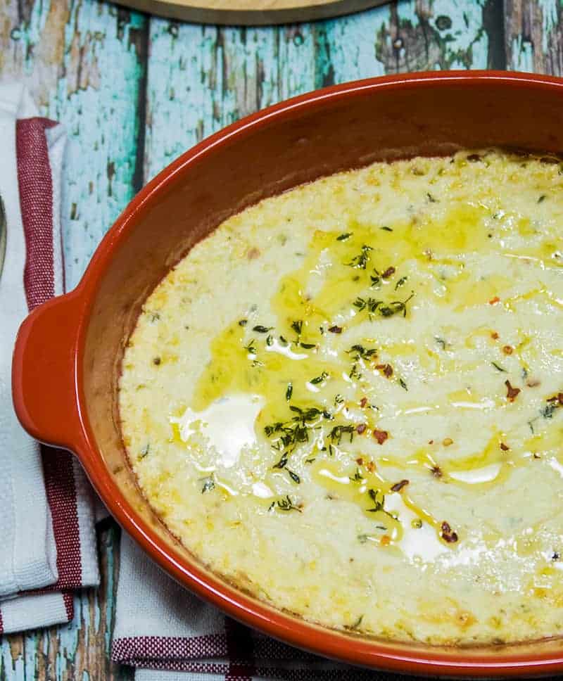  Baked Ricotta Cheese in an a red oval baking dish garnished with extra olive oil, fresh thyme and red chili pepper flakes