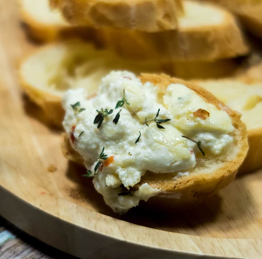  Baked Ricotta Cheese spread on a slice of a baguette garnished with fresh thyme.