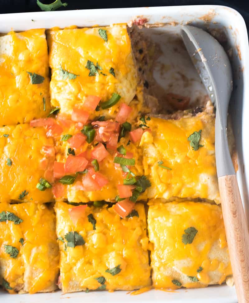 Taco Casserole topped with melted cheese, chopped tomato, jalapeno, and cilantro with one serving scooped out.