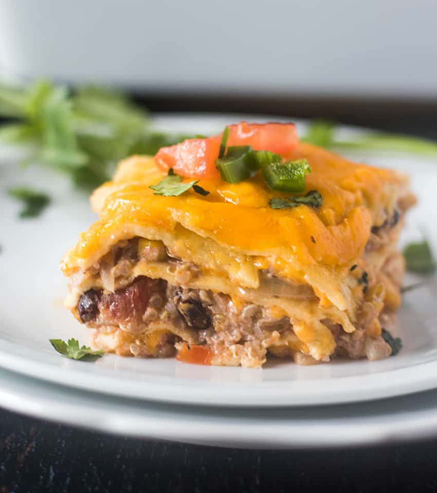 Single Square of Taco Casserole on a white place topped with chopped tomatoes, jalapeno and cilantro.