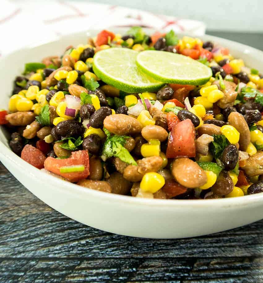 Black Bean corn salad i n a white bowl garnished with lime slices and fresh cilantro.