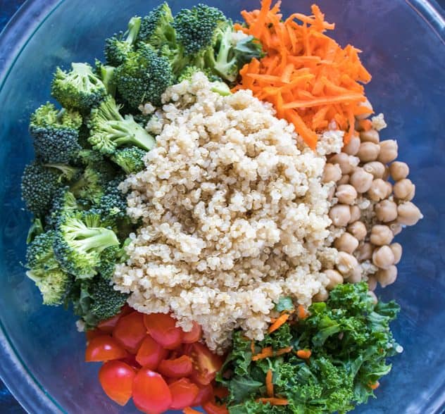 chopped kale, chickpeas, shredded carrots, chopped broccoli, chopped cherry tomatoes, and cooked quinoa in clear glass bowl.
