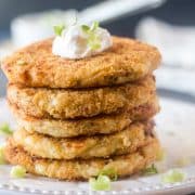 Mashed Potato Cakes stacked on a white plate topped with sour cream & green onions.