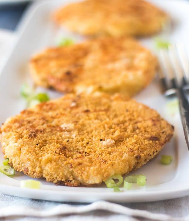 Three Mashed Potato Cakes on a long plate with green onions and a fork.