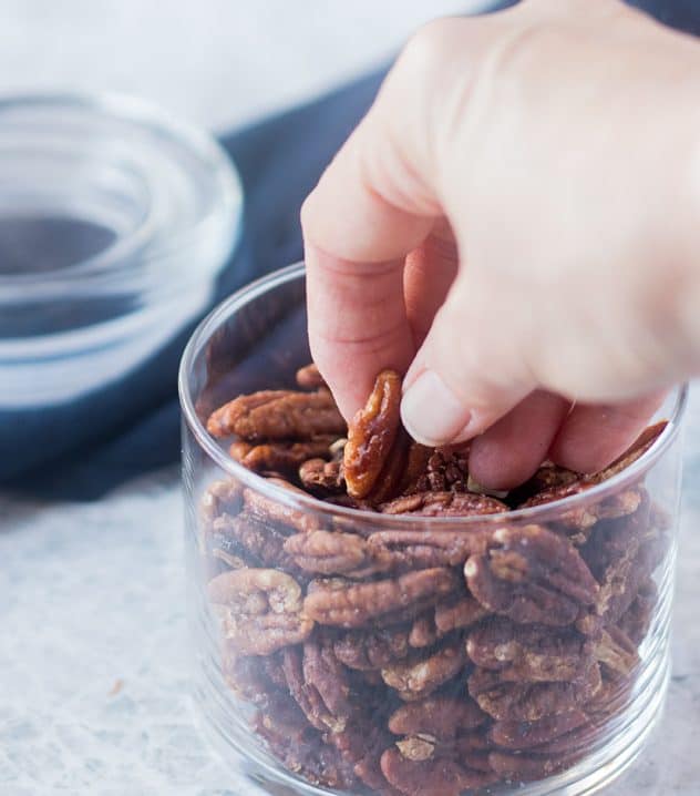 Hand reaching into a jar full of Maple Cinnamon Roasted Pecans.