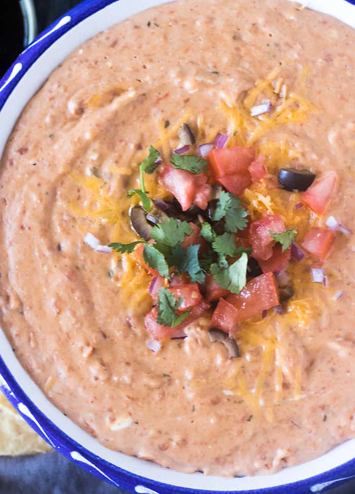 Bean dip in a bowl topped with chopped tomato, red onion, black olives and cilantro.