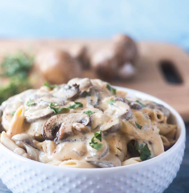 Mushroom Stroganoff topped on penne pasta served in a white bowl.