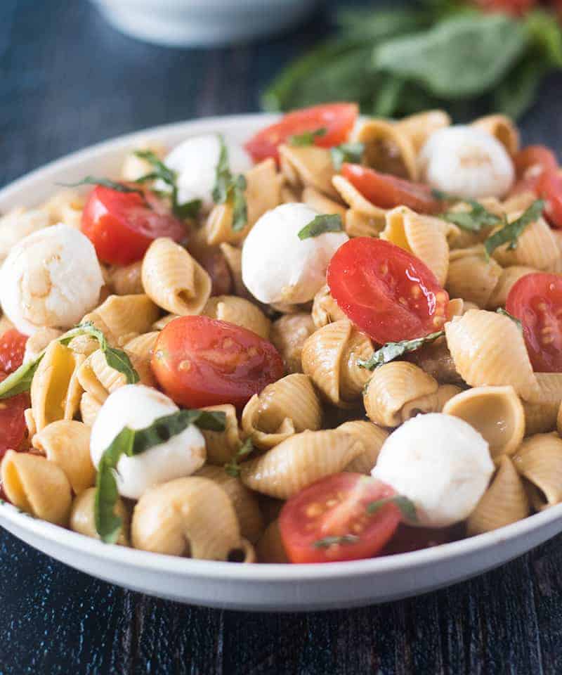 Caprese Pasta Salad in a white bowl with basil in background.