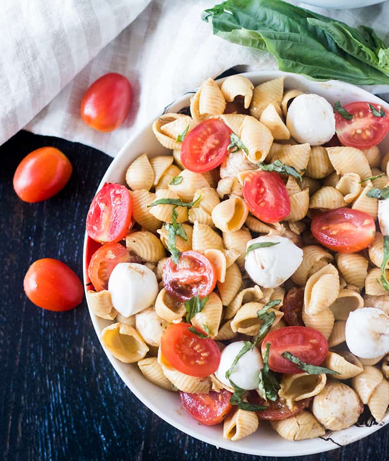 Caprese Pasta Salad in a white bowl with grape tomatoes beside it.
