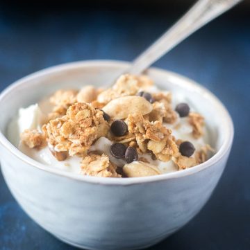 Peanut Butter Granola Clusters topped on greek yogurt in a white bowl with a silver spoon.