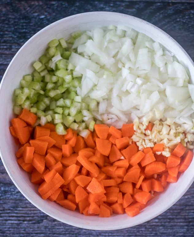 Chopped carrots, celery, sweet onion, and garlic in a white bowl.