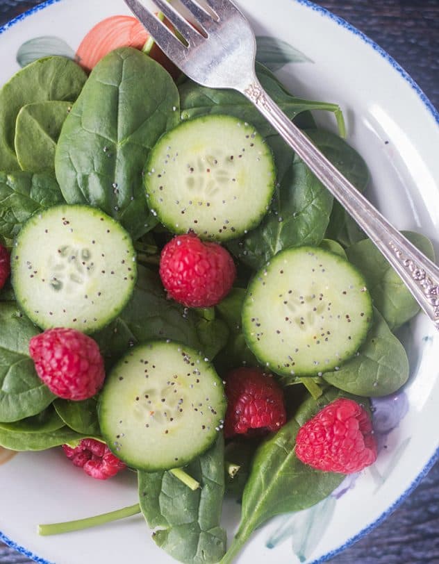 Spinach, cucumbers, raspberries in a white bowl with a fork.