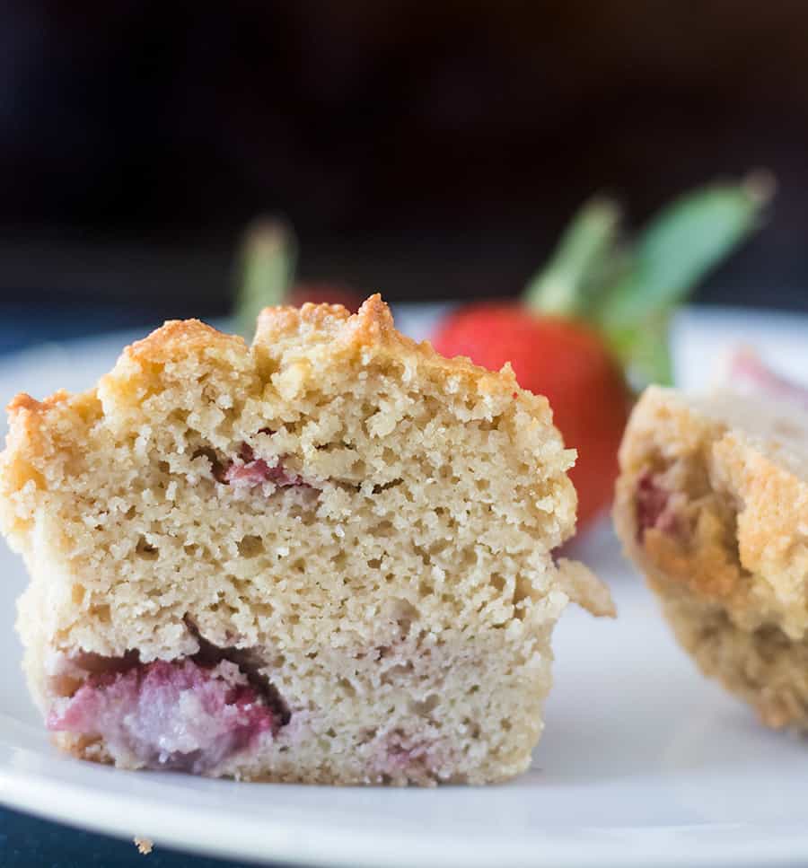 Strawberry Muffin cut in half on a white plate with fresh strawberry in the background.