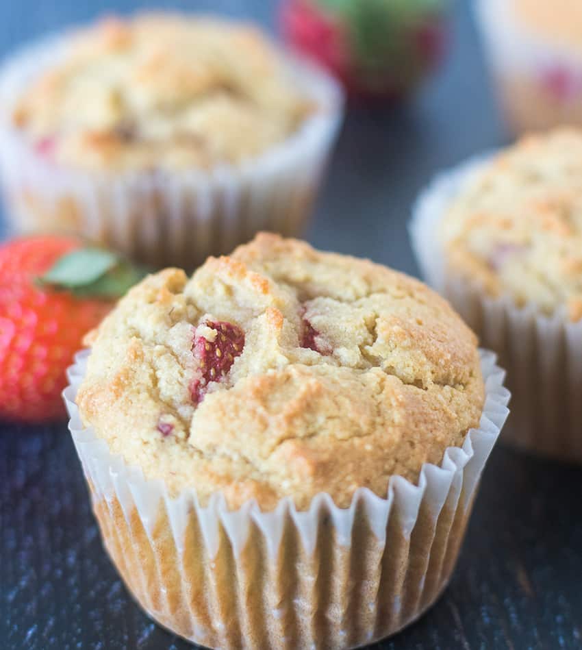 Strawberry Muffins in a baking cup with fresh strawberries in the background.