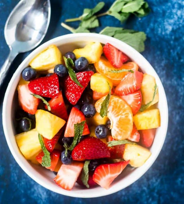 Summer fruit salad in a white bowl with mint leaves beside it and a silver spoon.
