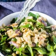 Caramelized Cabbage & Warm Spinach Salad in a white bowl with silver serving spoons.
