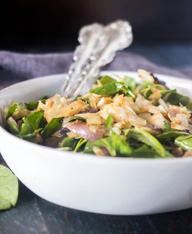 Caramelized Cabbage and Spinach salad in a white bowl with silver serving utensils.