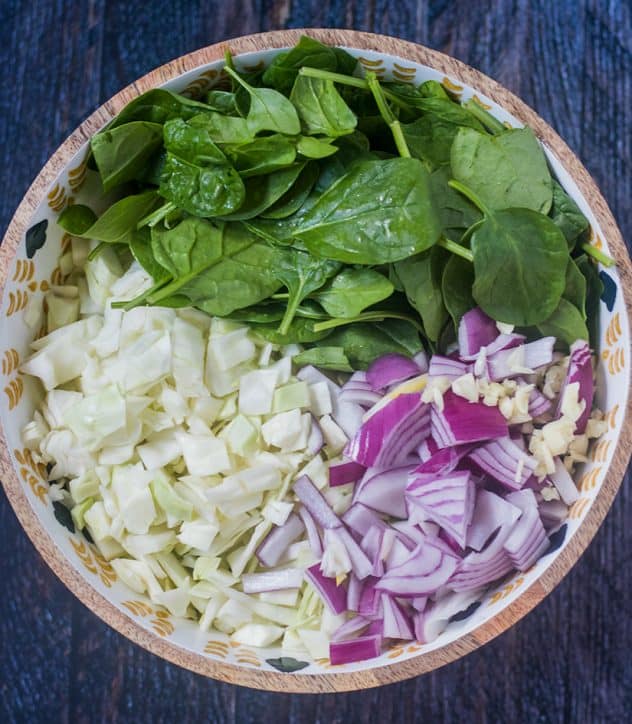 Chopped green cabbage, chopped red onion, chopped garlic and spinach in a large salad bowl.