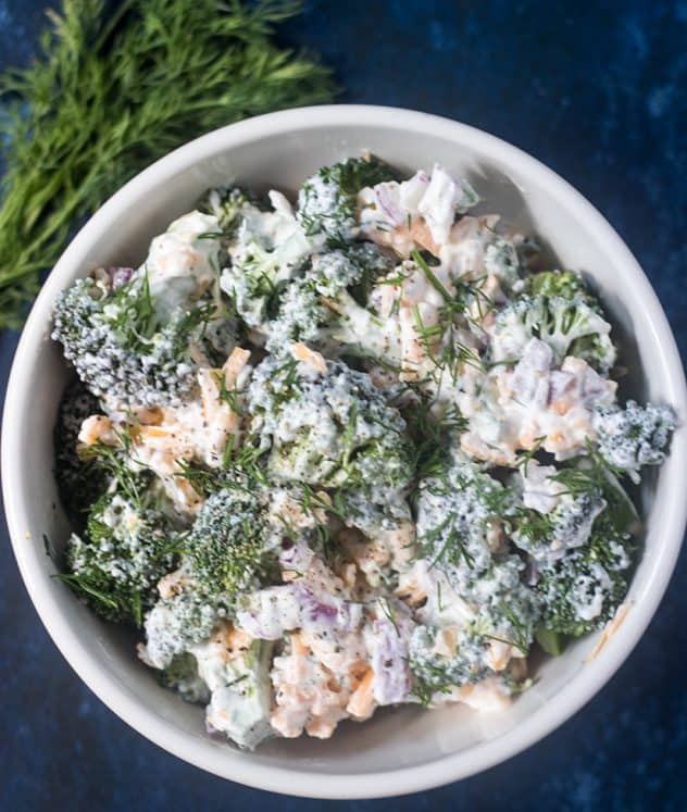 Broccoli Salad in a white bowl with fresh dill weed beside it.