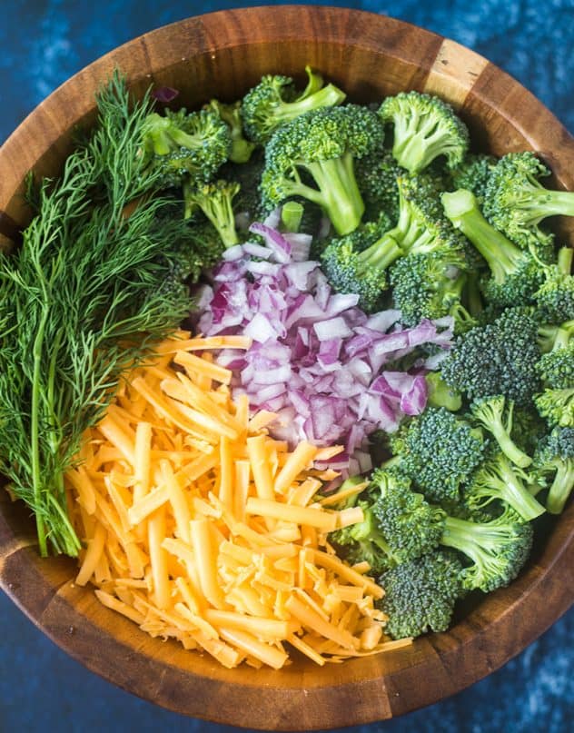 broccoli florets, red onion, cheddar cheese and dill weed in a salad bowl.