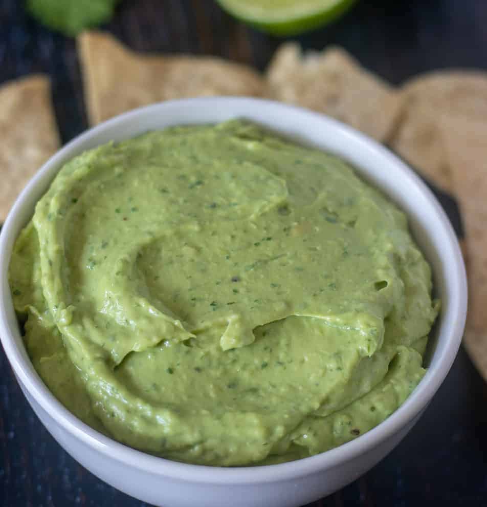 Avocado Dip in a white bowl with tortilla chips beside it.