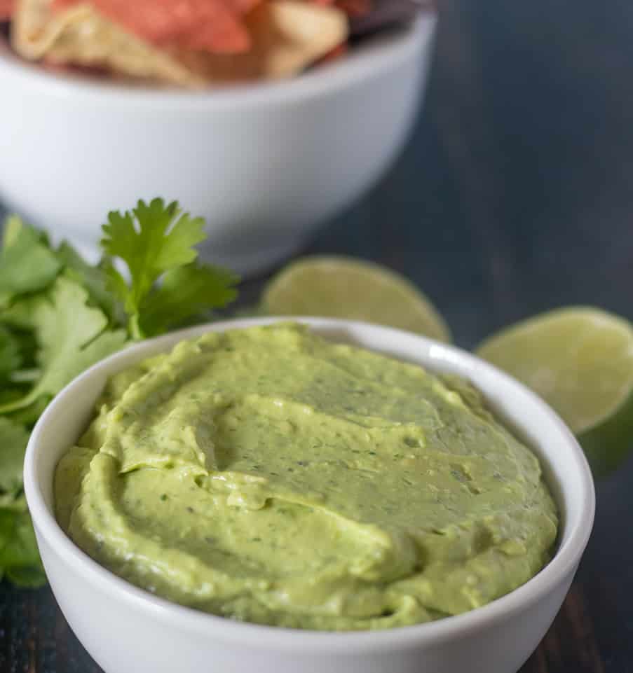 Avocado dip in a white bowl with chips in background.