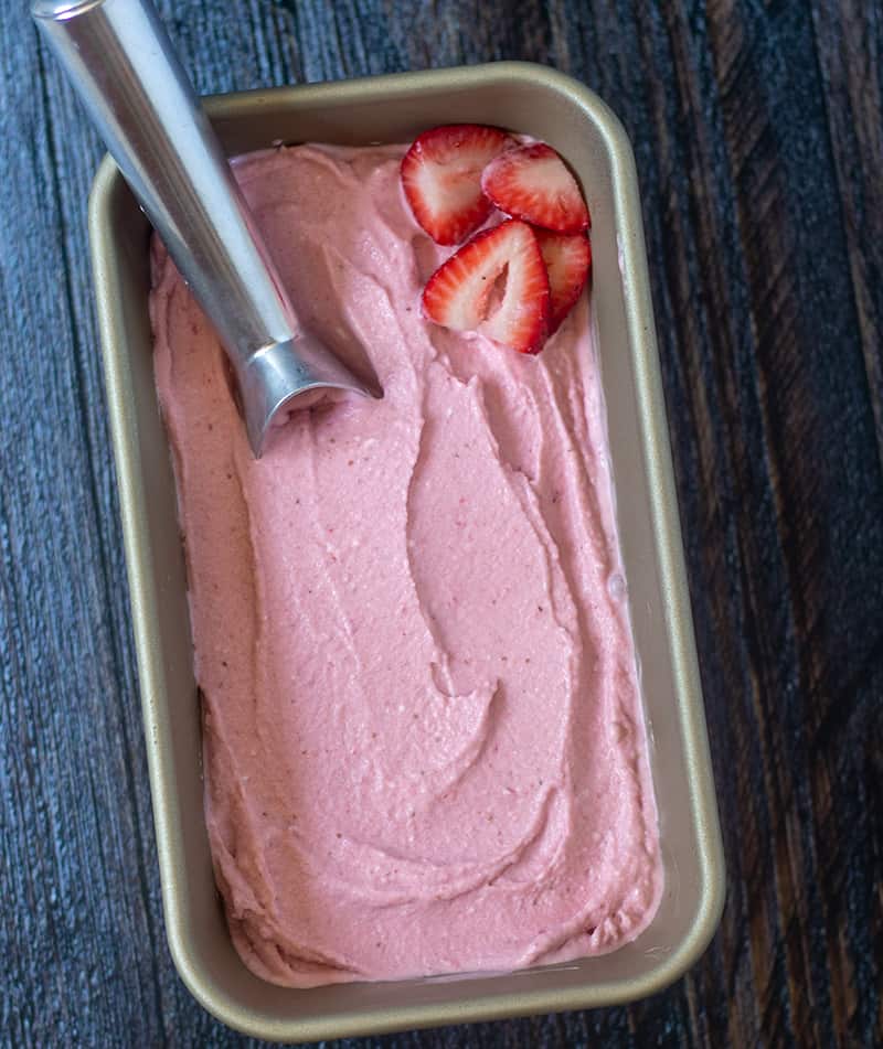 Paleo Strawberry Ice Cream in a loaf pan with ice cream scoop and chopped strawberries.