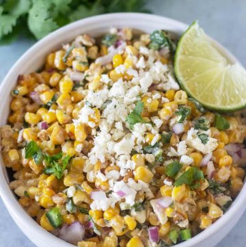Mexican Street Corn Salad in a bowl topped with feta cheese and a lime wedge.