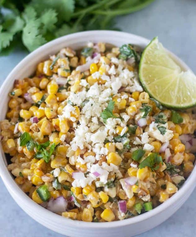 Mexican Street Corn Salad in a bowl topped with feta cheese and a lime wedge.