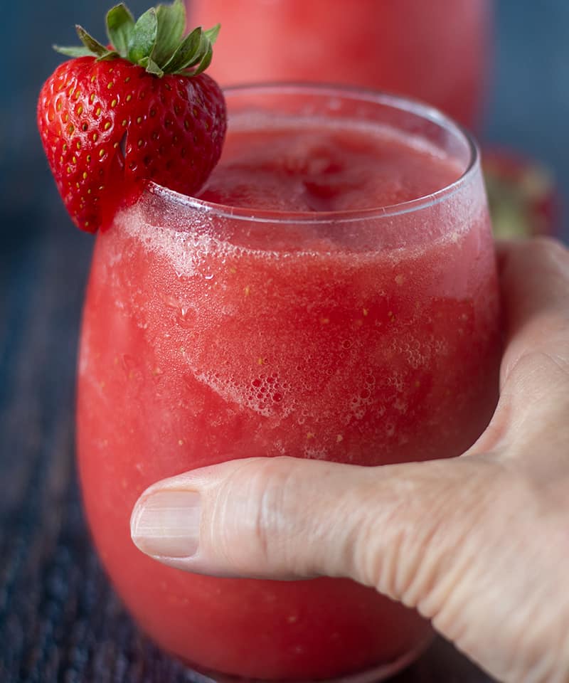 Watermelon Strawberry Wine Slushies in a glass and holding one with hand.