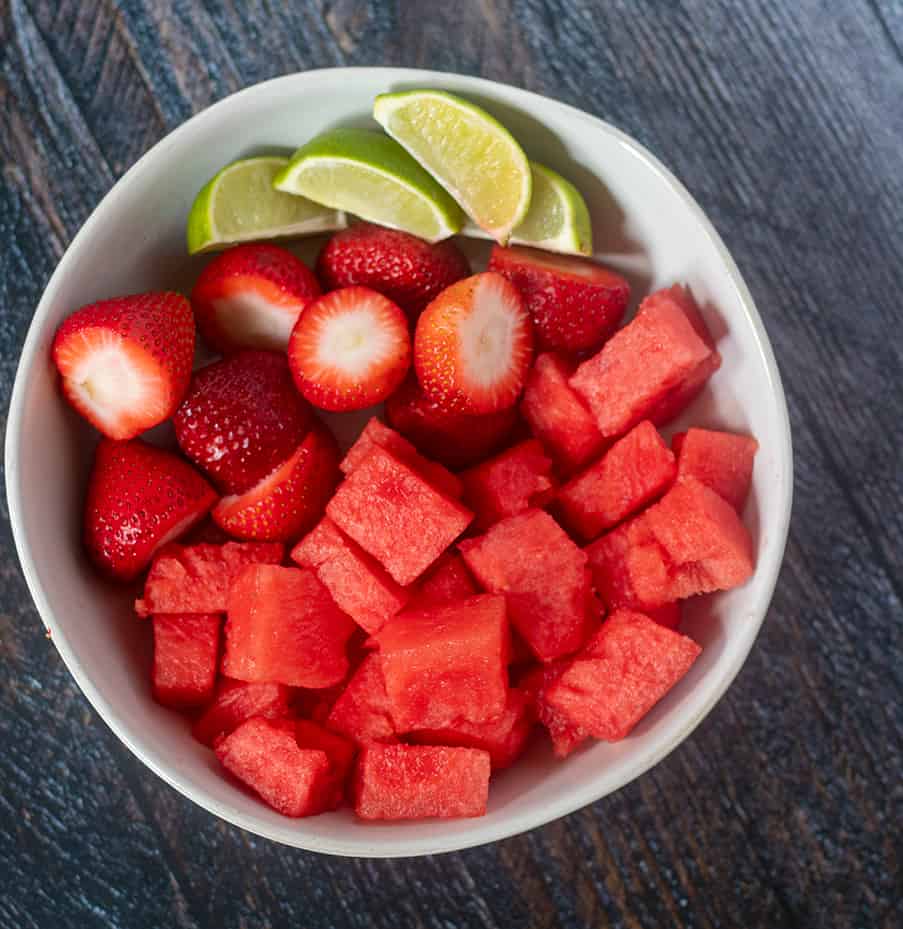 Watermelon chunks, strawberries and lime wedges in a white bowl.