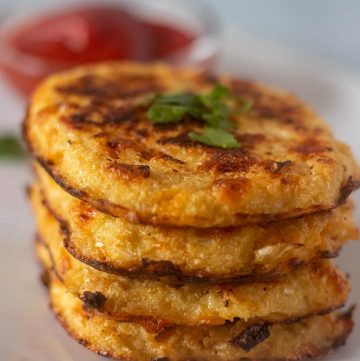 Cauliflower Hash Browns stacked on a plate with ketchup in a bowl.