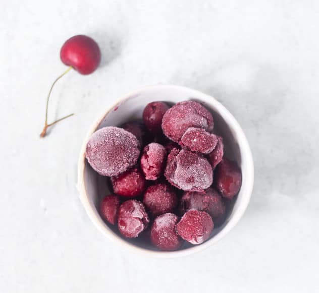 Frozen cherries in a white bowl with a fresh cherry beside it.