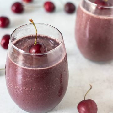 Cherry Smoothie in a glass topped with a fresh cherry and cherries in the background.