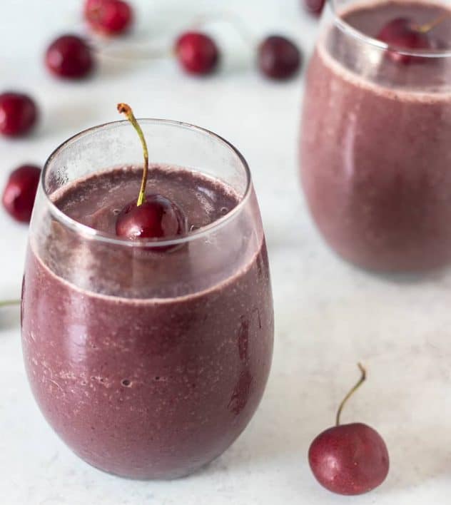 Cherry Smoothie in a glass topped with a fresh cherry and cherries in the background.