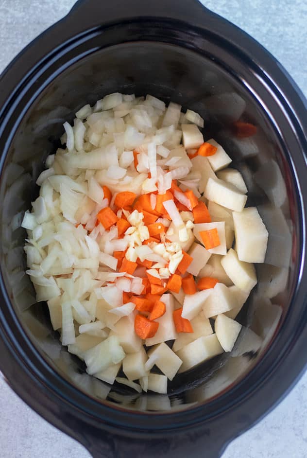 Diced potatoes, carrots, onions and garlic in a slow cooker.