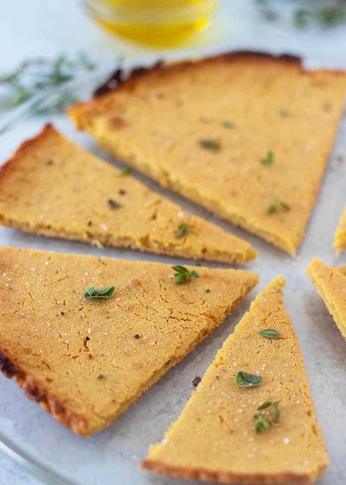 Socca on a serving plate garnished with fresh herbs.