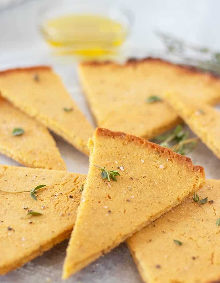 Socca on a plate cut in wedges with fresh herbs and a bowl of olive oil for dipping.