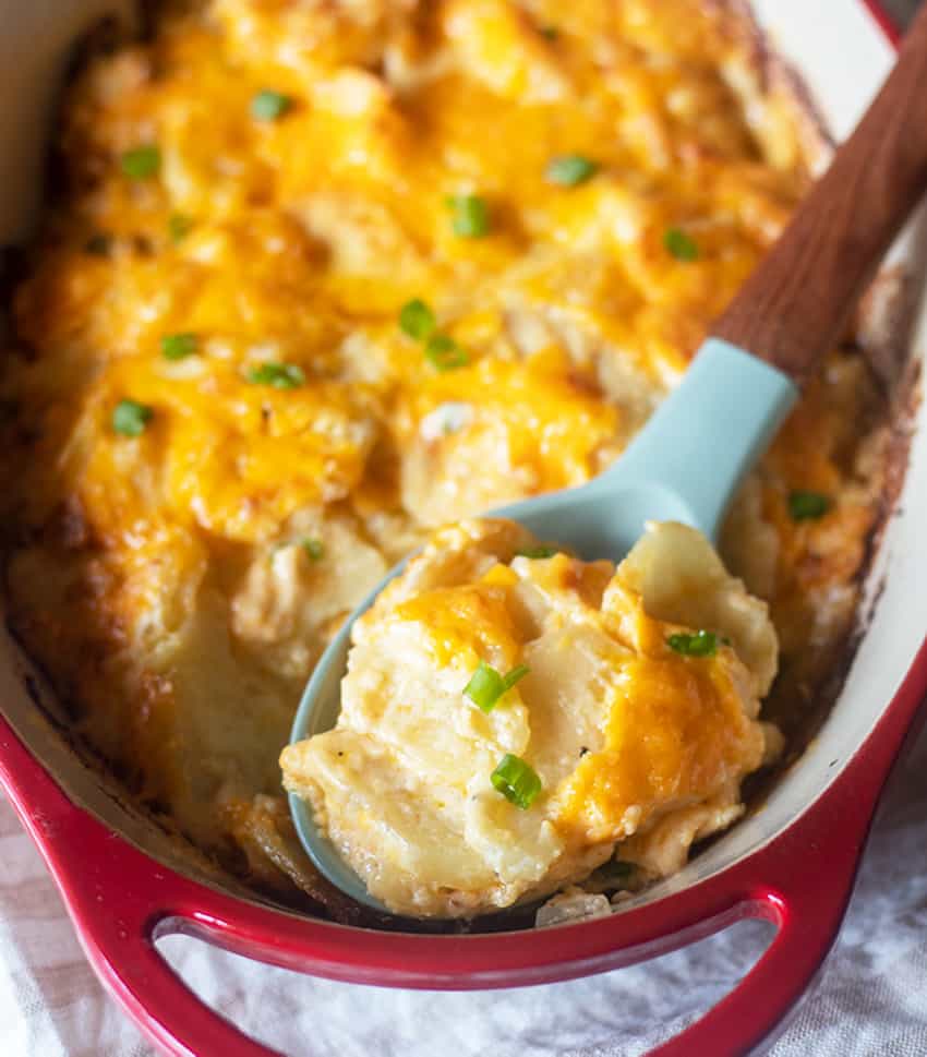 cheesy scalloped potatoes in a casserole pan with a spoon