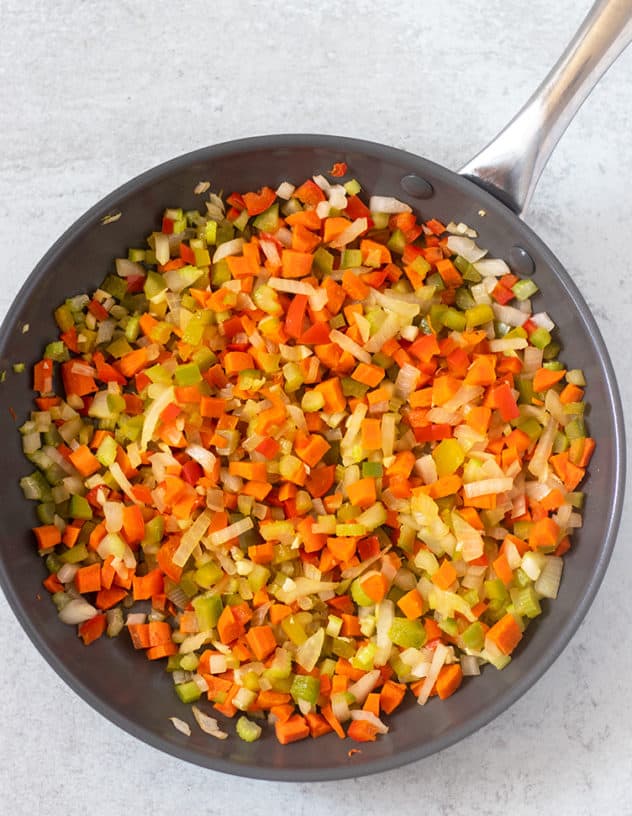 onion, carrots, celery, bell peppers sautéed in a pan.