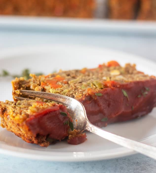 Slice of lentil loaf on a white plate with a silver fork.