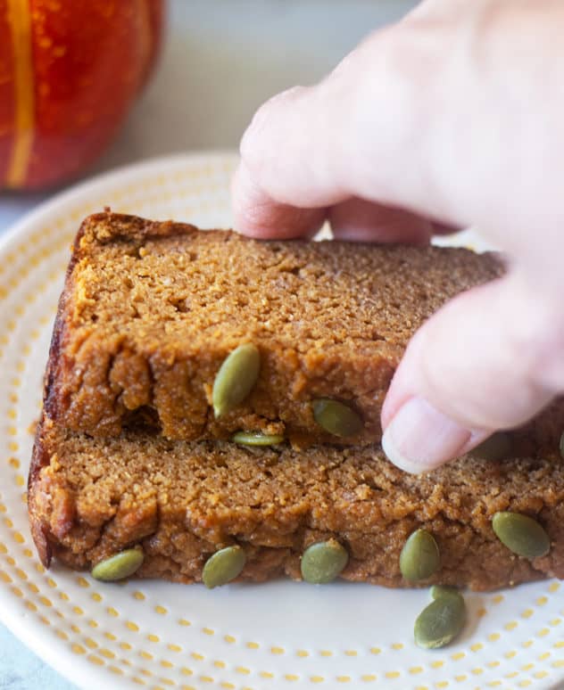 Paleo pumpkin bread on a plate and reaching for a slice.