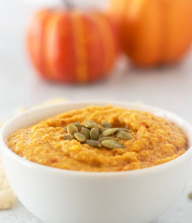 pumpkin hummus in a white bowl topped with pumpkin seeds