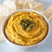 pumpkin hummus in a white bowl topped with pumpkin seeds and served with tortilla chips.