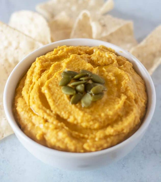 pumpkin hummus in a white bowl topped with pumpkin seeds and served with tortilla chips.