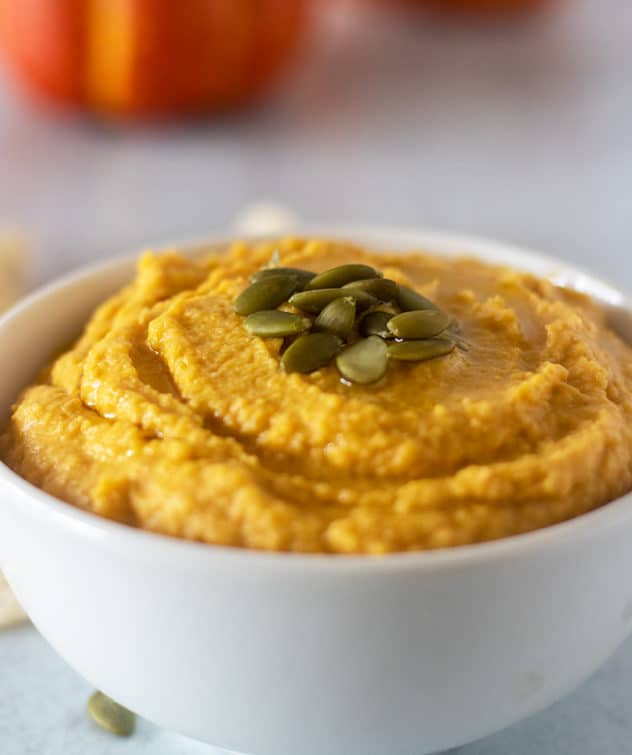 pumpkin hummus in a white bowl topped with pumpkin seeds